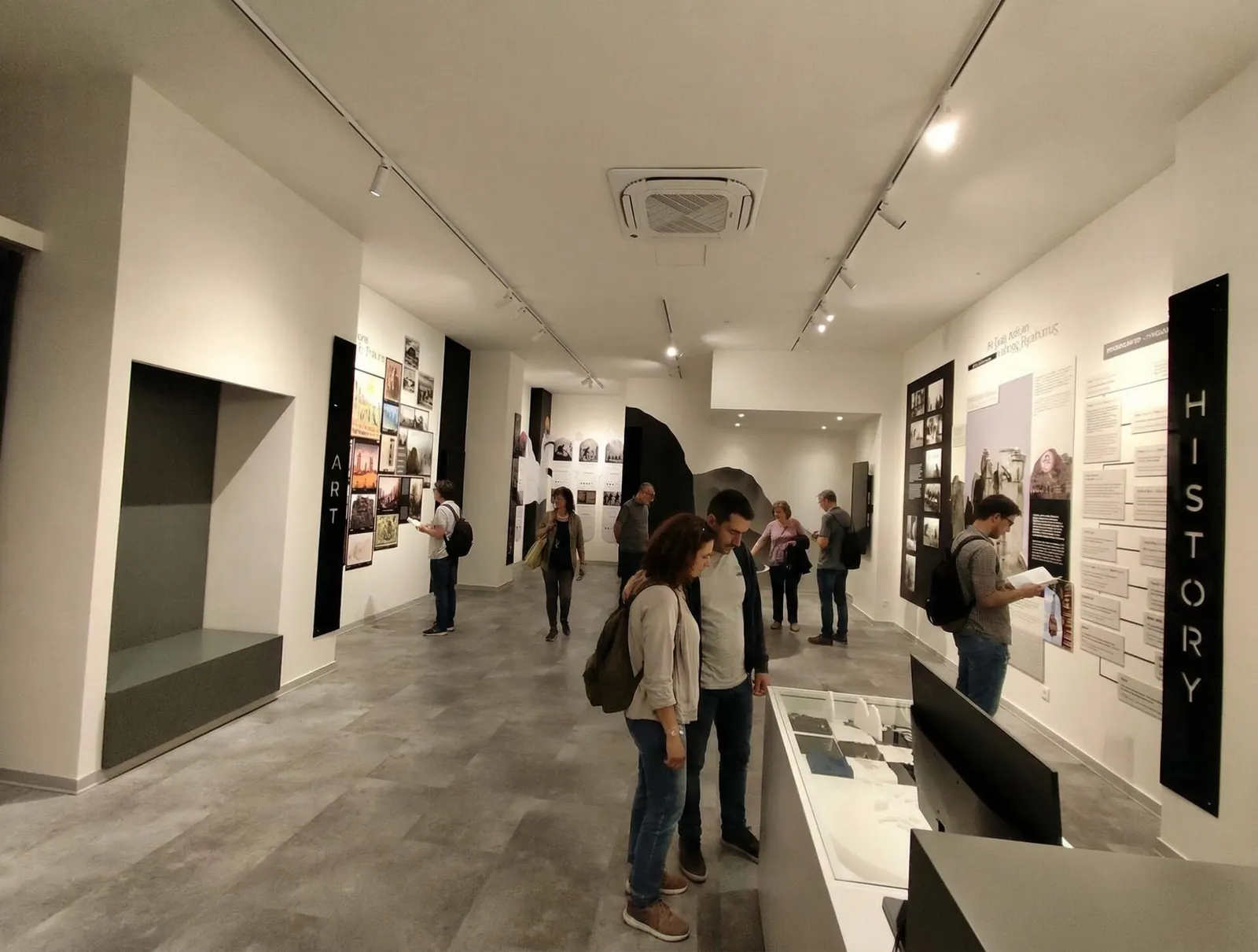 Επισκέπτες περιηγούνται στον φωτεινό εκθεσιακό χώρο του Terra Immersia, ανάμεσα σε φωτογραφίες και κείμενα στους τοίχους.